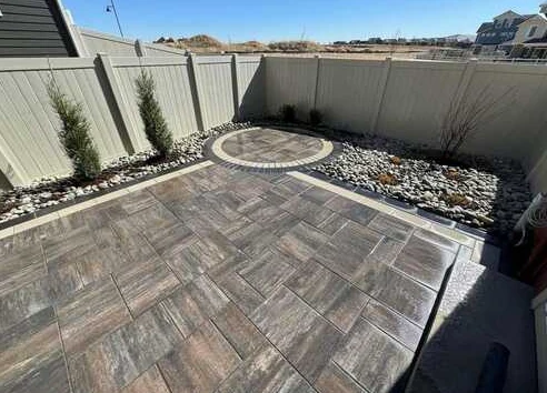 Multitone paver patio with contrasting borders and circular accent framed by rock beds.