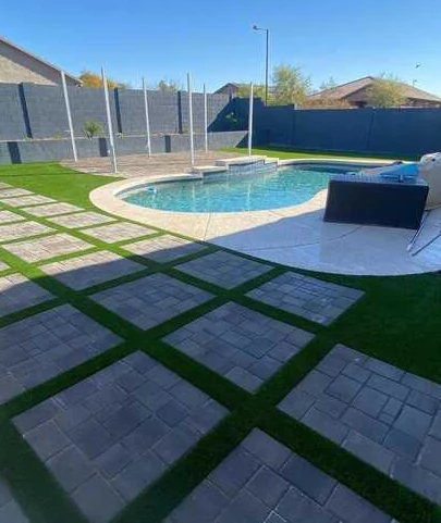 Finished square paver panels separated by turf beside a curved swimming pool.